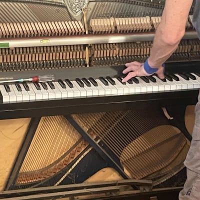 אדם מכוון פסנתר עם מכסה פתוח וכלי עבודה