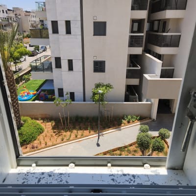נוף עירוני עם בניין וגינה דרך חלון פתוח