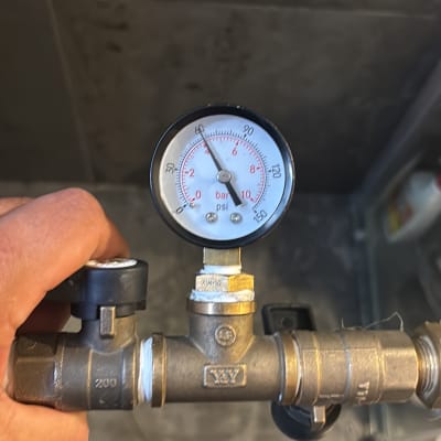 מד לחץ מים מוחזק ביד על רקע רצפה אפורה