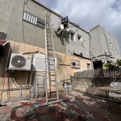 אדם עובד בגובה על קיר חיצוני עם סולם