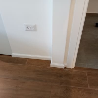 רצפת פרקט חומה ליד קיר לבן ושקע חשמל