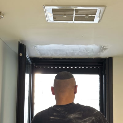 אדם עובד על תריסים בחדר עם פתח אוורור בתקרה