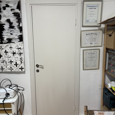 דלת לבנה עם ידית מתכת כסופה על קיר לבן