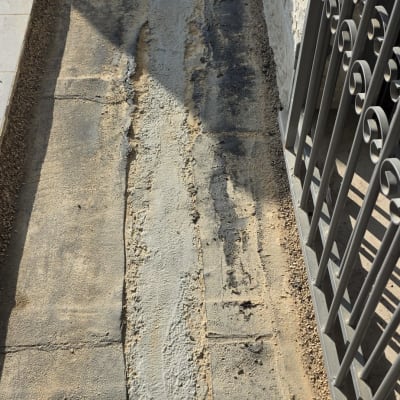 משטח בטון עם סימני איטום ליד גדר מתכת