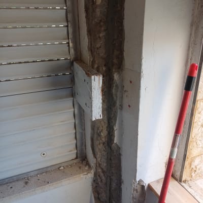 קיר מתקלף עם טיח חשוף ליד חלון בתהליך שיפוץ