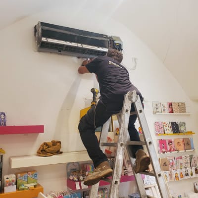 טכנאי מתקין מזגן על קיר בעזרת סולם