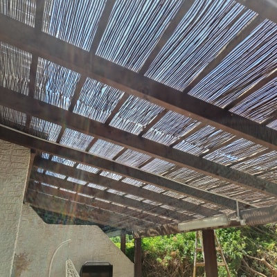 פרגולה מעץ עם גג קנים מעל גינה