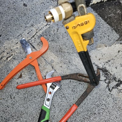 כלי עבודה וצנרת על רצפה, כולל מפתח צינורות