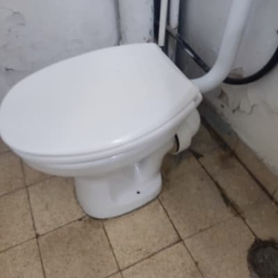 אסלה לבנה עם צינורות מים על קיר מתקלף