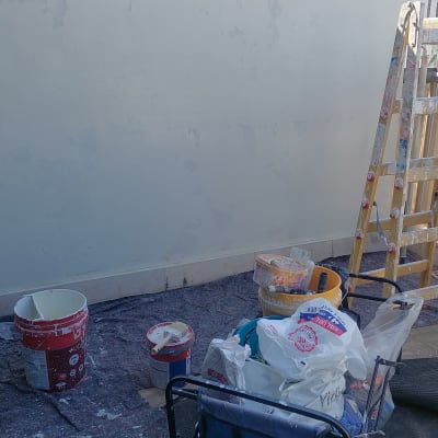 ציוד צביעה, דליי צבע וסולם לצד קיר בתהליך הכנה לצביעה