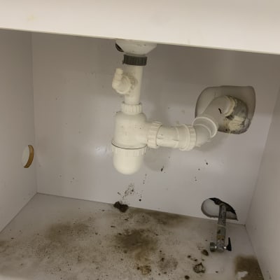 צנרת פלסטיק מתחת לכיור עם לכלוך על הרצפה