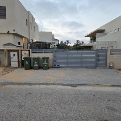 חצר עם שער וגדר, פחי אשפה ובתים ברקע