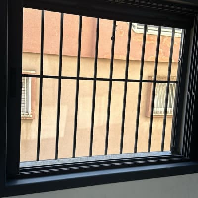 חלון עם סורגים שחורים על רקע קיר חיצוני