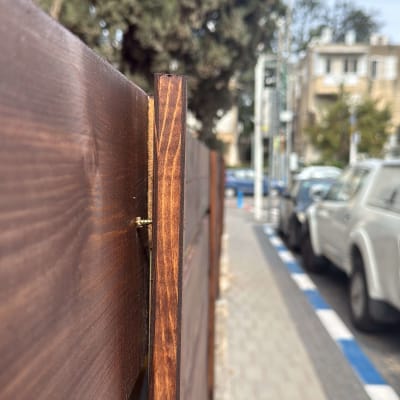 גדר עץ חומה לצד מדרכה ועצים ברקע