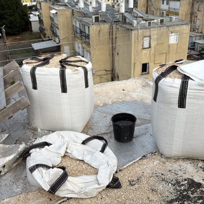 שקי חצץ על גג בניין עם משטח עץ ודלי שחור