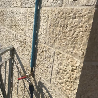 ברז מים עם צינור כחול על קיר אבן