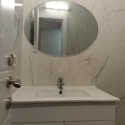 מראה עגולה מעל כיור בחדר אמבטיה עם קיר שיש