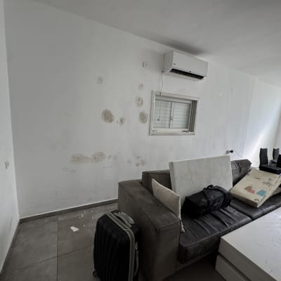 קיר עם כתמי צבע ותיקונים, ספה ושולחן בסלון