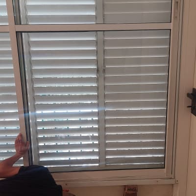 אדם עובד על תריסי אלומיניום בחלון פנימי