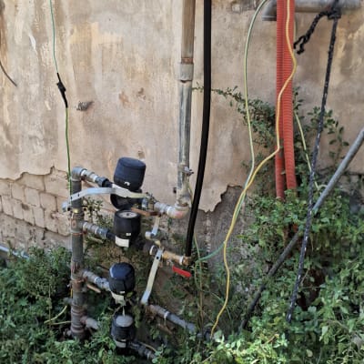 צינורות ומדי מים מחוברים לקיר חיצוני עם צמחייה סביבם