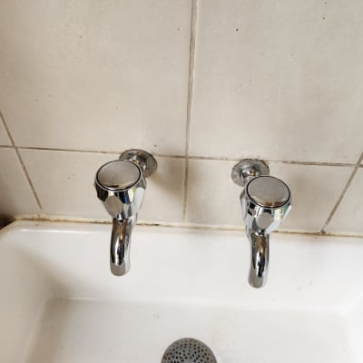 ברזים כפולים מעל כיור לבן עם ניקוז