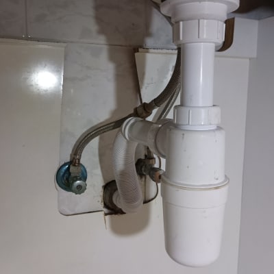 צנרת מתחת לכיור עם ברזים וצינור פלסטיק