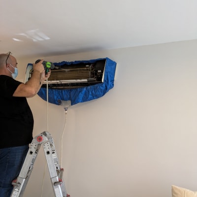 טכנאי מנקה מזגן עם כיסוי כחול על סולם