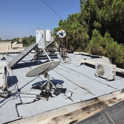 גג עם אנטנות ומזגן, עצים ברקע