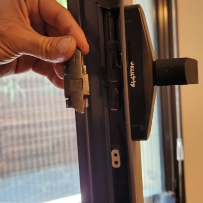 יד מחזיקה חלק מתכת ליד חלון עם תריסים