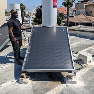 אדם בודק דוד שמש על גג עם קולטים סולאריים.