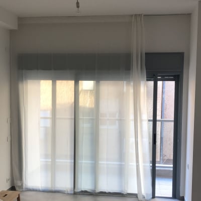 וילון לבן תלוי על מסילה מעל חלון זכוכית