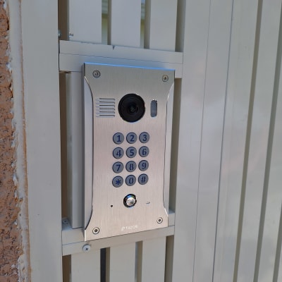 אינטרקום עם מצלמה ולוח מקשים על שער מתכת