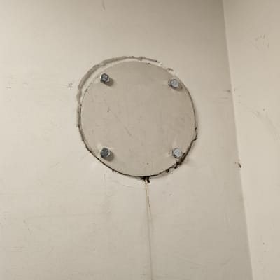 קיר עם חור עגול מכוסה בלוח מתכת וברגים