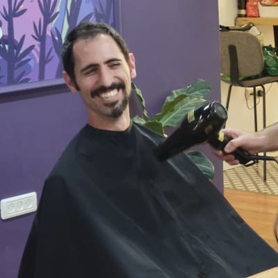 אדם מחייך עם חלוק מספרה ומייבש שיער