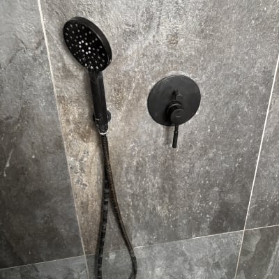 ראש מקלחת שחור עם צינור על קיר אפור