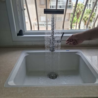 ברז מים זורם מעל כיור במטבח עם חלון ברקע