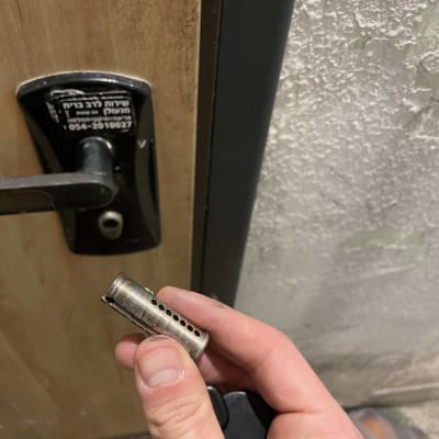 יד מחזיקה צילינדר מנעול מול דלת עץ