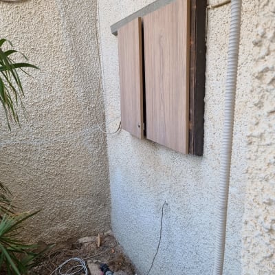 ארון עץ מותקן על קיר חיצוני עם צינורות חשמל
