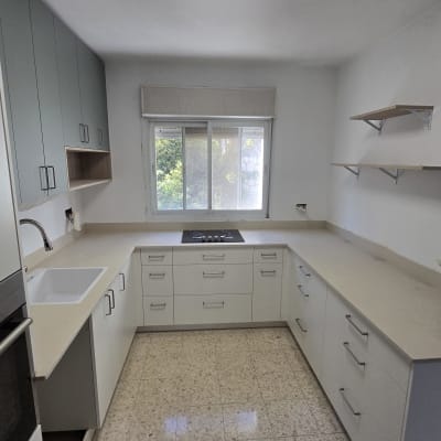 מטבח מודרני מותקן עם ארונות ישרים בגוונים בהירים ומשטח עבודה