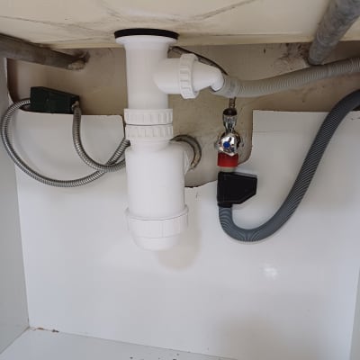 צנרת פלסטיק לבנה מתחת לכיור עם ברזים וצינורות