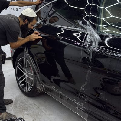 אדם מבצע עבודת דיטיילינג על רכב שחור עם כלים מקצועיים