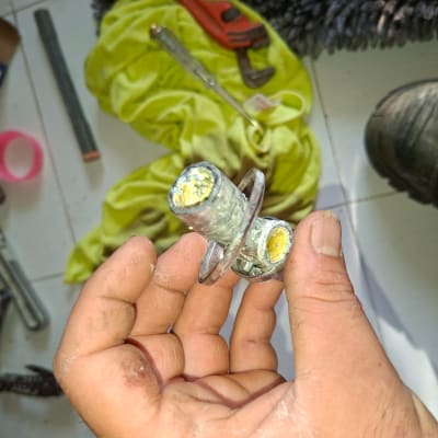 כלי עבודה וצנרת על הרצפה, יד מחזיקה חלק מתכת