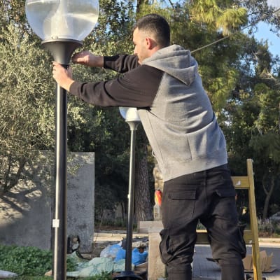 אדם מתקין מנורה על עמוד תאורה בחוץ