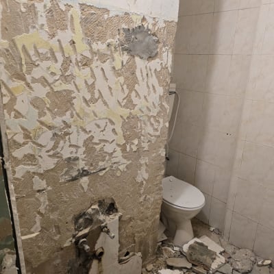 חדר אמבטיה בהריסה עם קיר מתקלף ופסולת על הרצפה