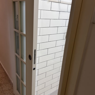 דלת זכוכית פתוחה עם קיר אריחים לבנים