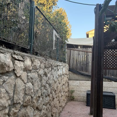 חצר בית עם חומת אבן, גדר ועצים שנגזמו מאחוריה