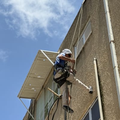 אדם עובד בגובה על קיר בניין עם ציוד בטיחות