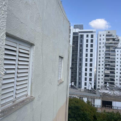 בניין מגורים עם חלונות ותריסים, רקע של שמיים כחולים ובניינים נוספים.