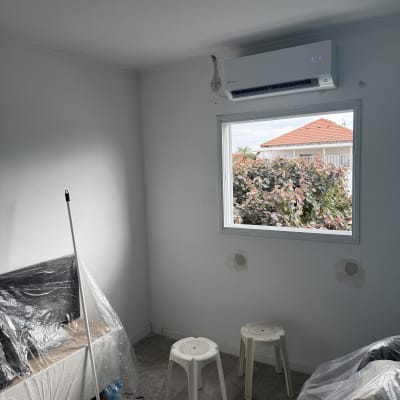 מזגן מותקן על קיר בחדר עם כיסאות פלסטיק ורצפה מכוסה בניילון