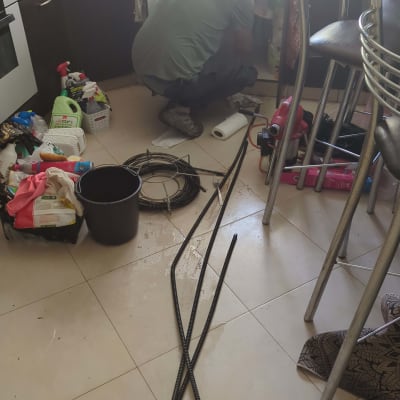 אדם מתקן צנרת מתחת לכיור במטבח